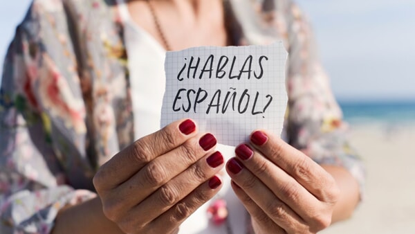 An older woman holds up a sign in front of her that asks ¿Hablas Español? 